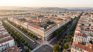 Vue aérienne réaliste de Montpellier montrant le centre historique, les quartiers modernes et les lignes de tramway sous une douce lumière méditerranéenne.